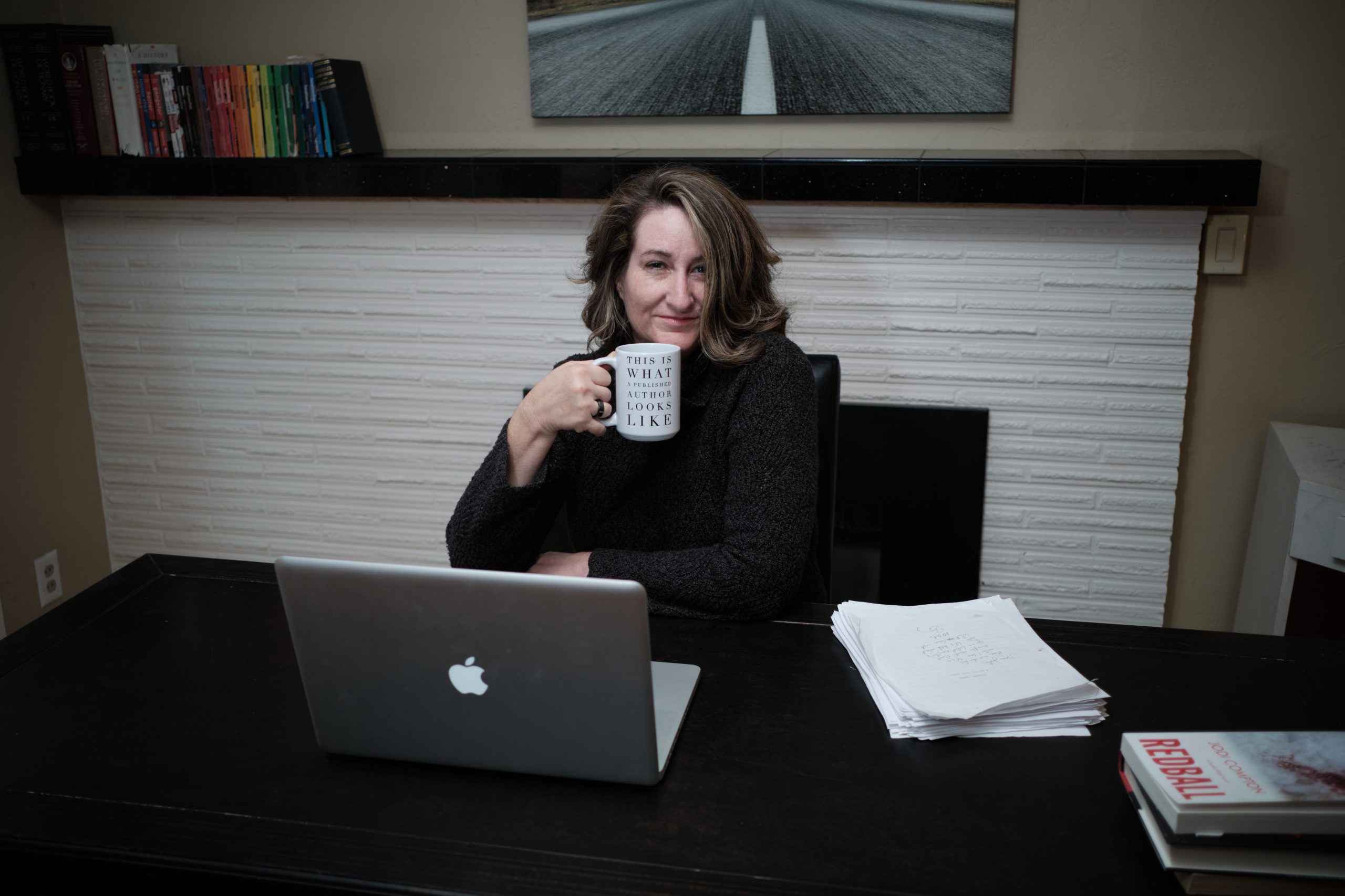 jodi compton at a long desk, holding coffe mug